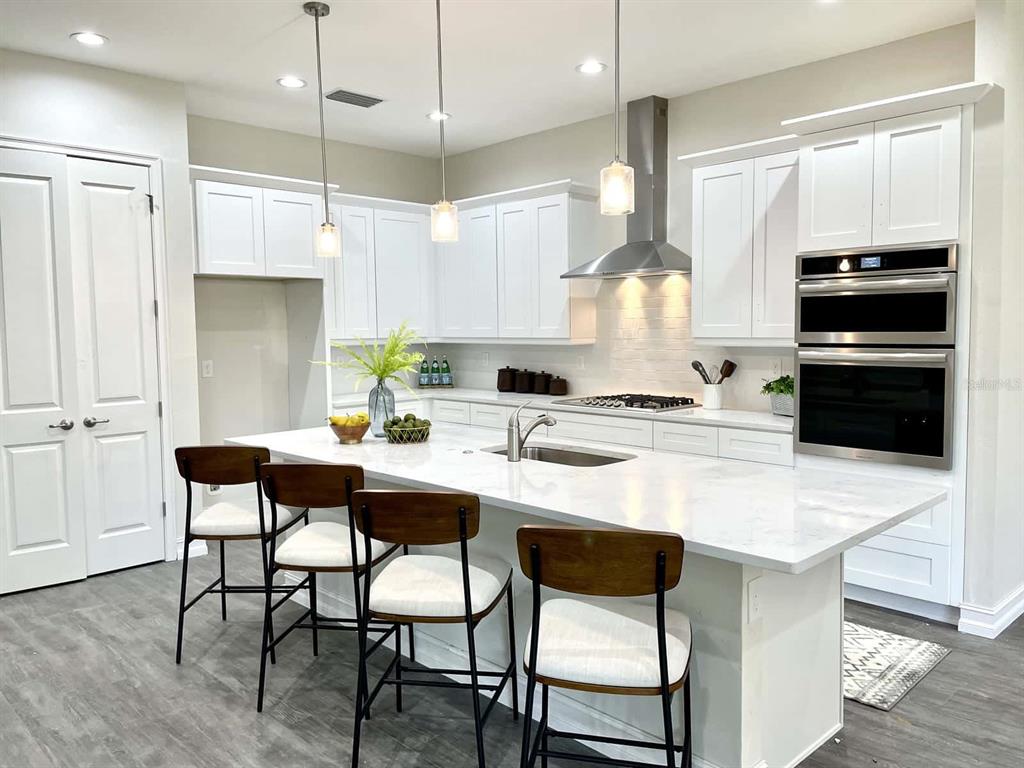 A modern kitchen features white cabinetry, a large marble-topped island, and stainless steel appliances — 4836 MAJESTIC HILLS LOOP, BROOKSVILLE, FL