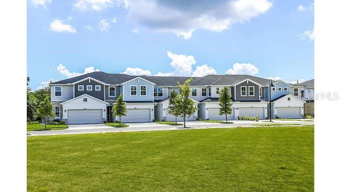 A row of multi-story townhomes with attached garages sits behind a large green lawn — 2626 HAM BROWN ROAD UNIT Emilia, KISSIMMEE, FL
