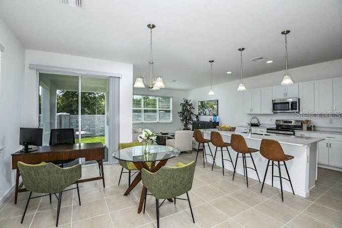 An open-concept kitchen and dining area features a glass-topped table, bar seating, and tile flooring — 2626 HAM BROWN ROAD UNIT Emilia, KISSIMMEE, FL