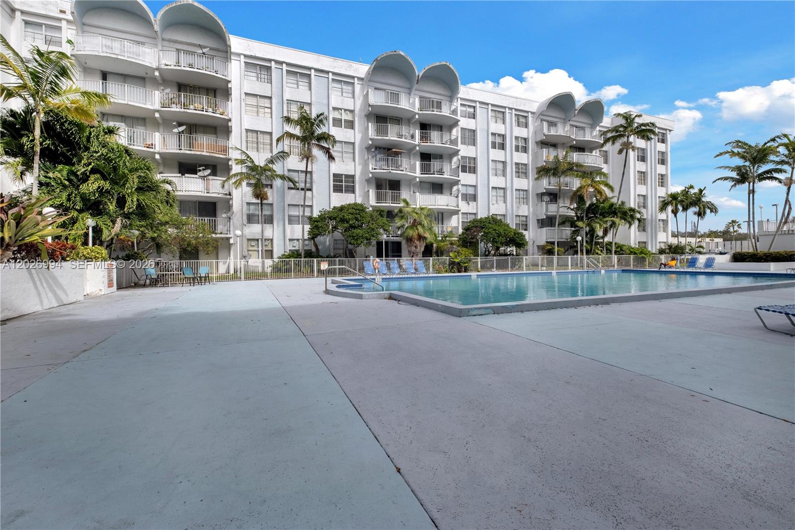 A large swimming pool sits in front of a multi-story white residential apartment building — 496 NW 165th St Rd # 616, Miami FL 33169, MIAMI, FL