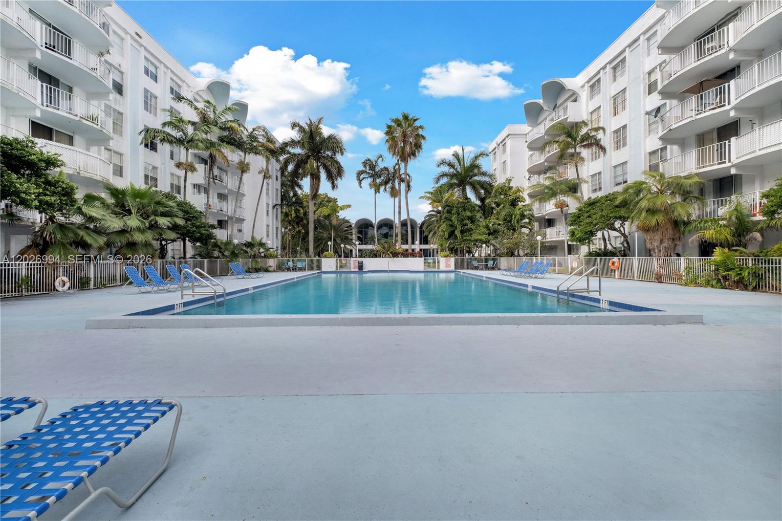 A rectangular swimming pool is centered between two white multi-story apartment buildings with palm trees — 496 NW 165th St Rd # 616, Miami FL 33169, MIAMI, FL