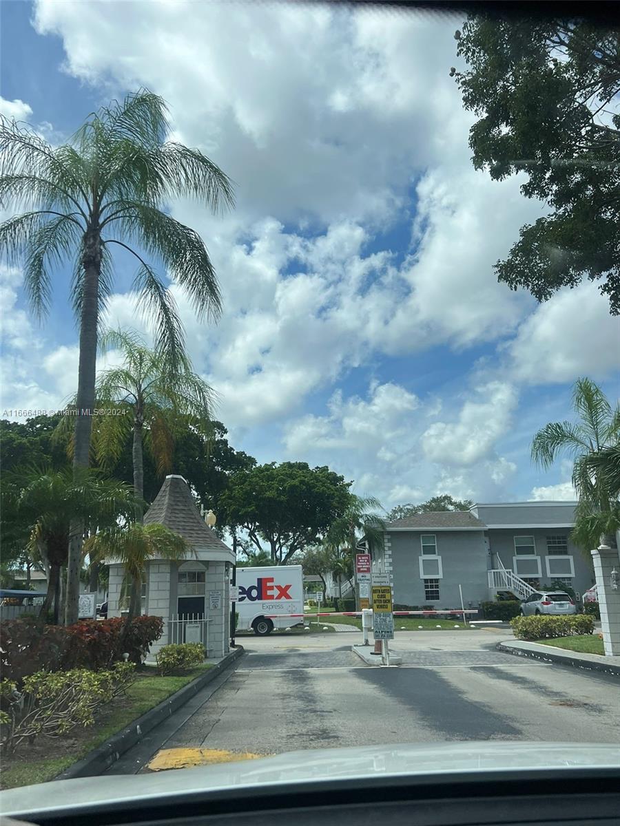 A gated entrance features a guardhouse, a FedEx truck, and palm trees under a cloudy sky — 435 NE 210th Cir Ter # 23, Miami FL 33179, MIAMI, FL