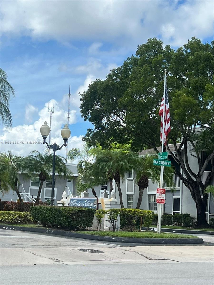 The exterior of Monterey Village features a street sign, an American flag, and landscaping — 435 NE 210th Cir Ter # 23, Miami FL 33179, MIAMI, FL
