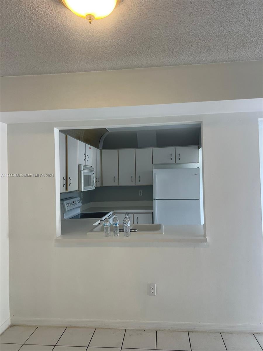 A kitchen with white cabinets and appliances is viewed through a pass-through window — 435 NE 210th Cir Ter # 23, Miami FL 33179, MIAMI, FL