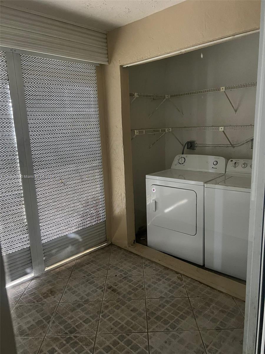 A laundry closet with a washer and dryer sits beside a room with tiled floors — 435 NE 210th Cir Ter # 23, Miami FL 33179, MIAMI, FL
