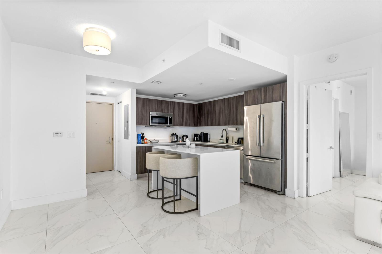 A modern kitchen features white marble floors, a central island, and dark wood cabinetry — 488 NE 18th Street # 905, Miami FL 33132, MIAMI, FL