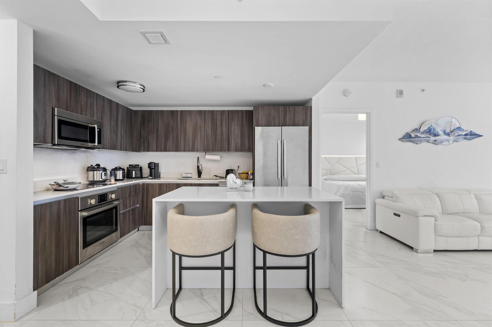 A modern kitchen features dark wood cabinets, stainless steel appliances, and a white island with stools — 488 NE 18th Street # 905, Miami FL 33132, MIAMI, FL