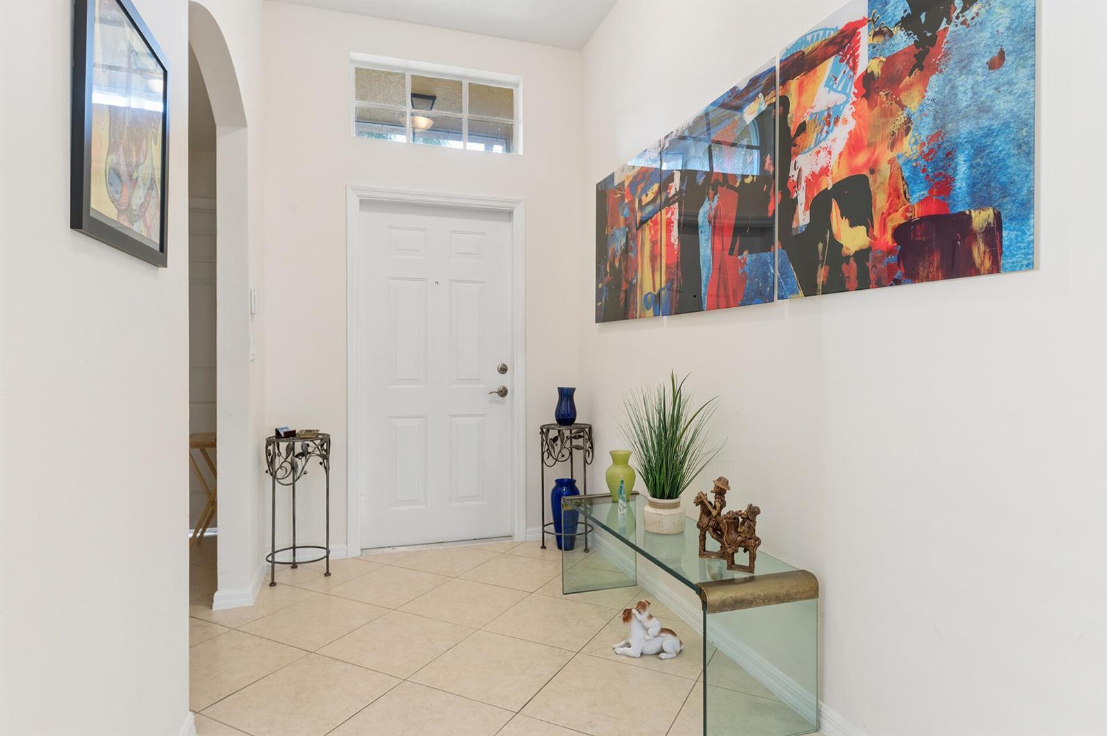 A bright entryway features tile flooring, a white front door, and colorful abstract wall art — 12024 Roma Road, Boynton Beach FL 33437, BOYNTON BEACH, FL