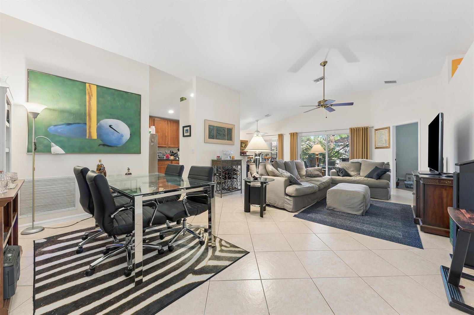 An open-concept living and dining area features tile flooring, a glass table, and neutral furniture — 12024 Roma Road, Boynton Beach FL 33437, BOYNTON BEACH, FL