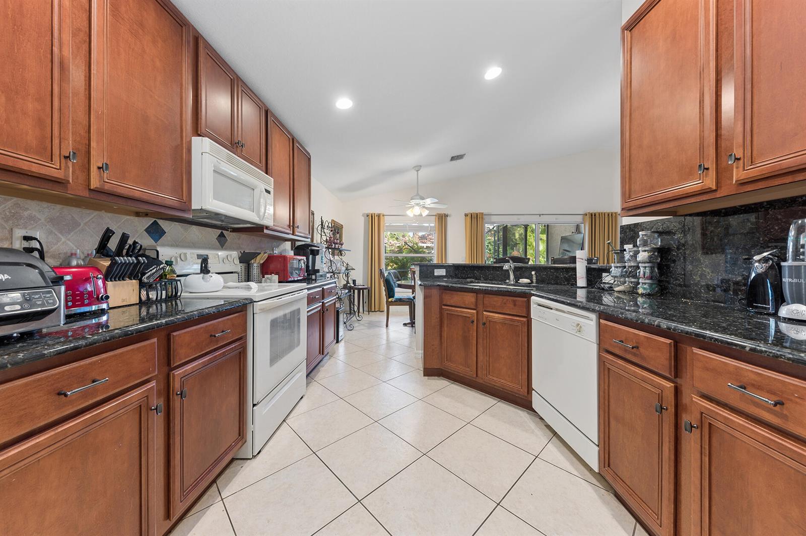 A kitchen features wood cabinets, dark granite countertops, white appliances, and light tile flooring — 12024 Roma Road, Boynton Beach FL 33437, BOYNTON BEACH, FL