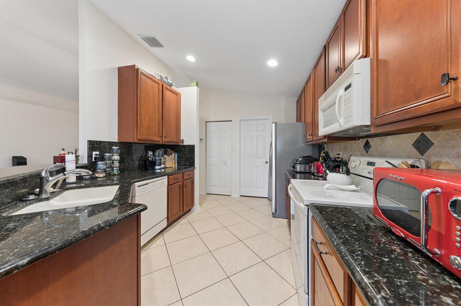 A kitchen features dark wood cabinets, black granite countertops, white appliances, and light tile flooring — 12024 Roma Road, Boynton Beach FL 33437, BOYNTON BEACH, FL