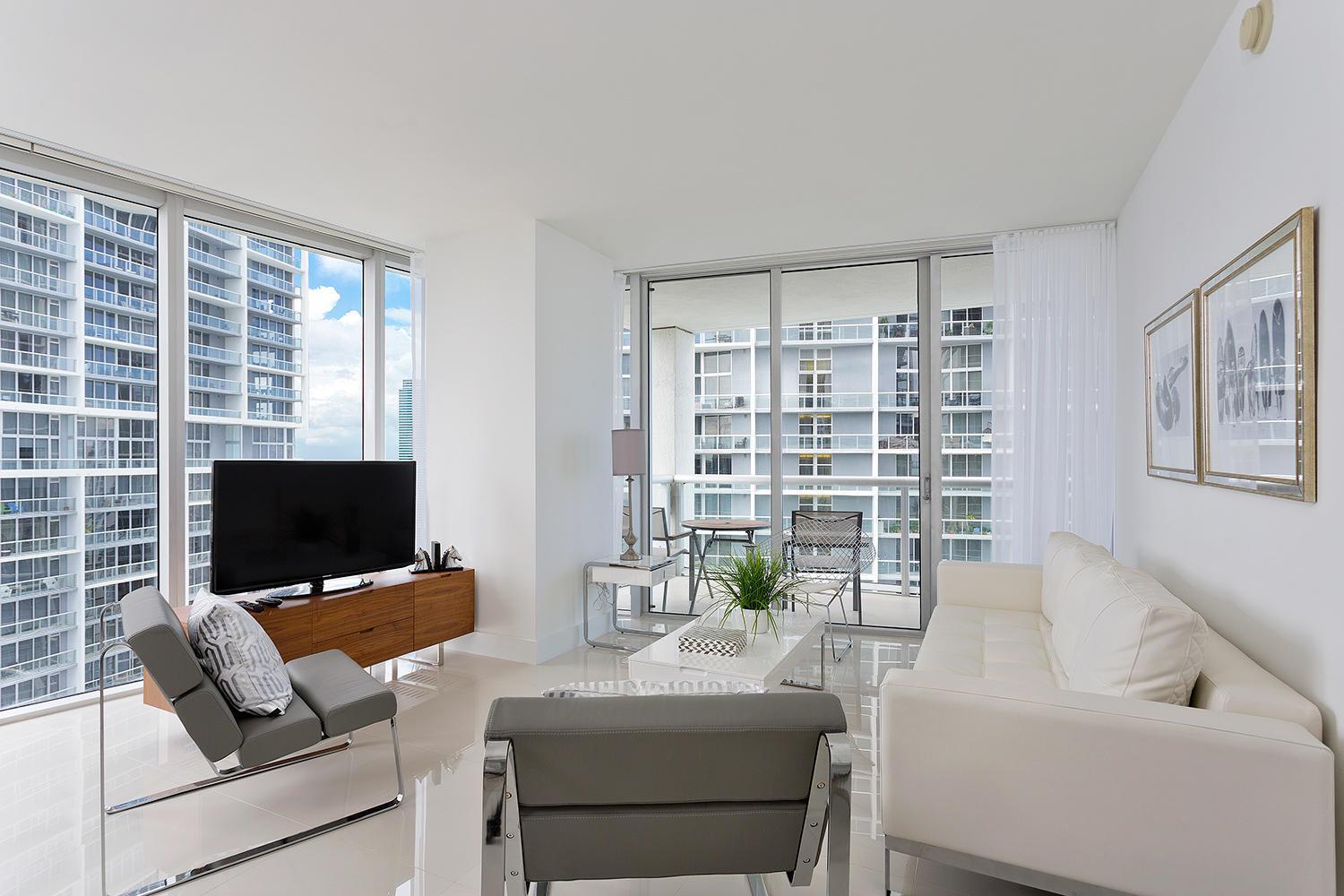 A modern living room features a white sofa, grey chairs, and floor-to-ceiling windows overlooking buildings — 495 Brickell Avenue # 4010, Miami FL 33131, MIAMI, FL