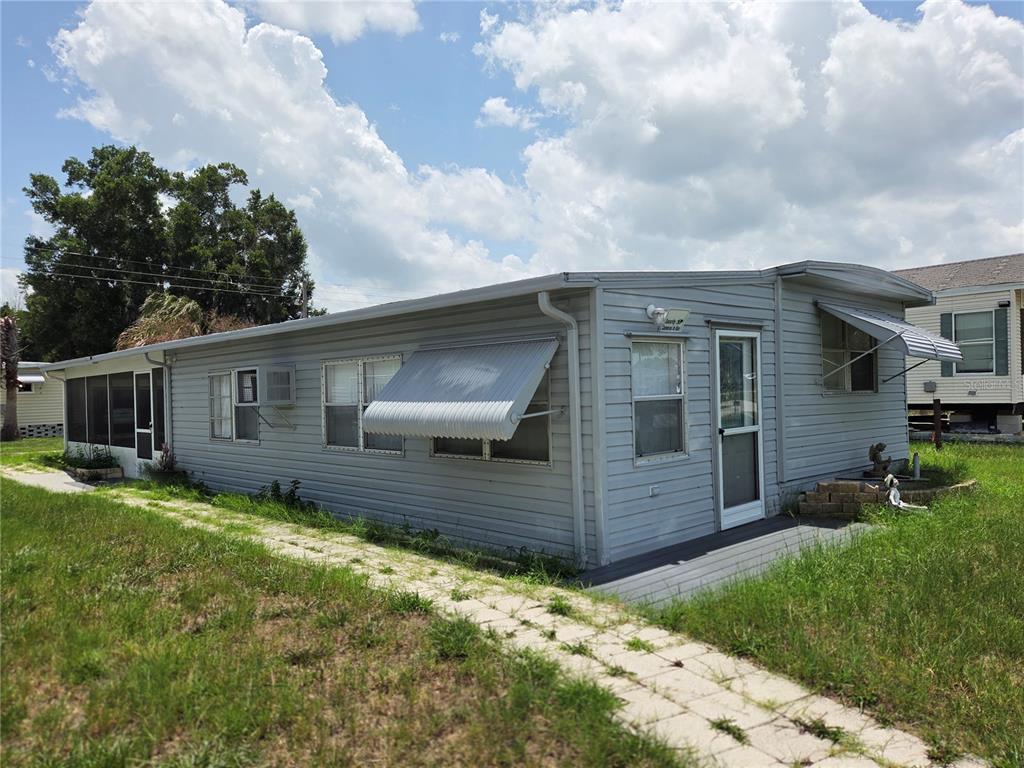 A light gray mobile home with a metal awning and a paved walkway in front — 6240 CONNECTICUT STREET, ZEPHYRHILLS, FL