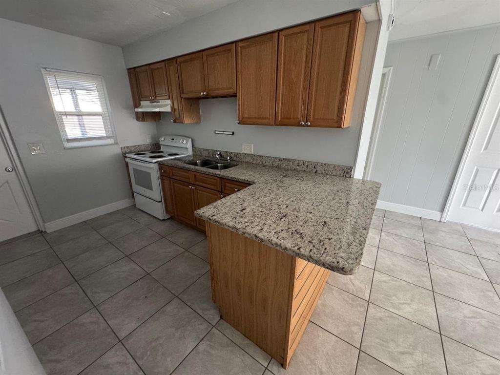A kitchen features wood cabinets, granite countertops, a white stove, and light-colored tile flooring — 1392 KING STREET UNIT 1392, BARTOW, FL