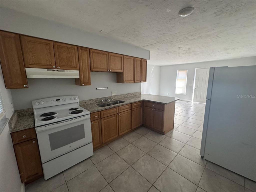 A kitchen features wood cabinets, granite countertops, a white stove, and tile flooring — 1392 KING STREET UNIT 1392, BARTOW, FL