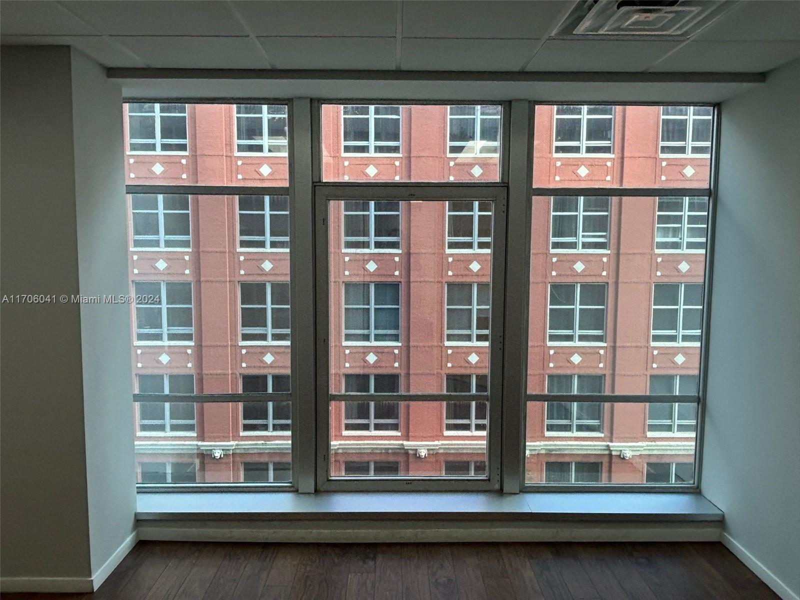 A room with dark wood flooring looks out through a large window at a brick building — 14 NE 1st Ave # 700D, Miami FL 33132, MIAMI, FL
