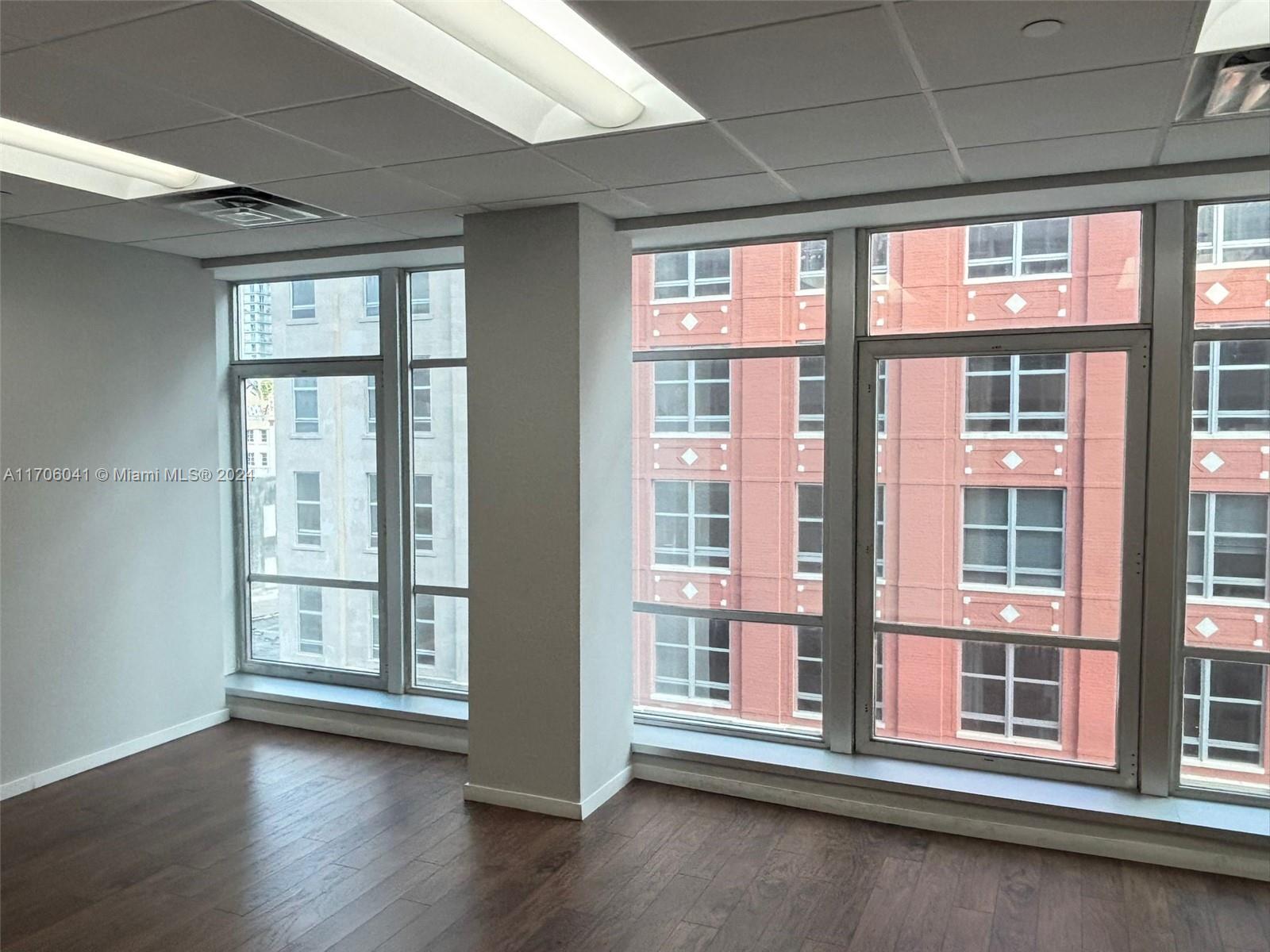 An empty office space features wood-look flooring, a drop ceiling, and large windows overlooking buildings — 14 NE 1st Ave # 700D, Miami FL 33132, MIAMI, FL