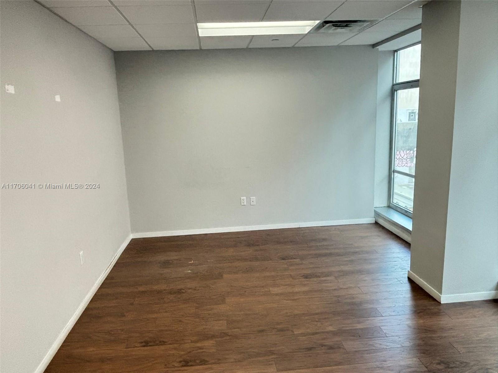 An empty office space features light gray walls, dark wood-look flooring, and a large window — 14 NE 1st Ave # 700D, Miami FL 33132, MIAMI, FL