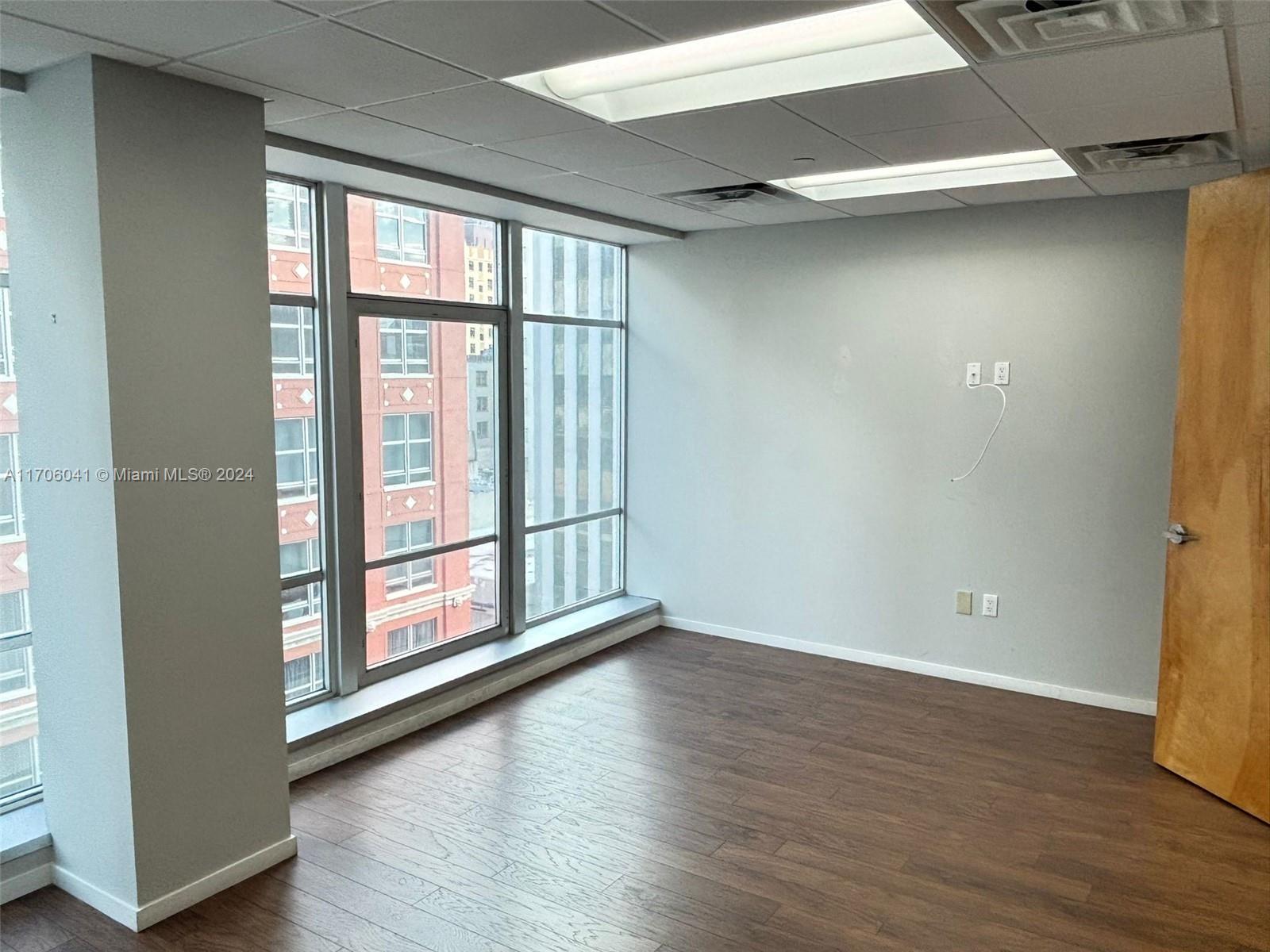 An empty office space features wood-look flooring, light gray walls, and large floor-to-ceiling windows — 14 NE 1st Ave # 700D, Miami FL 33132, MIAMI, FL