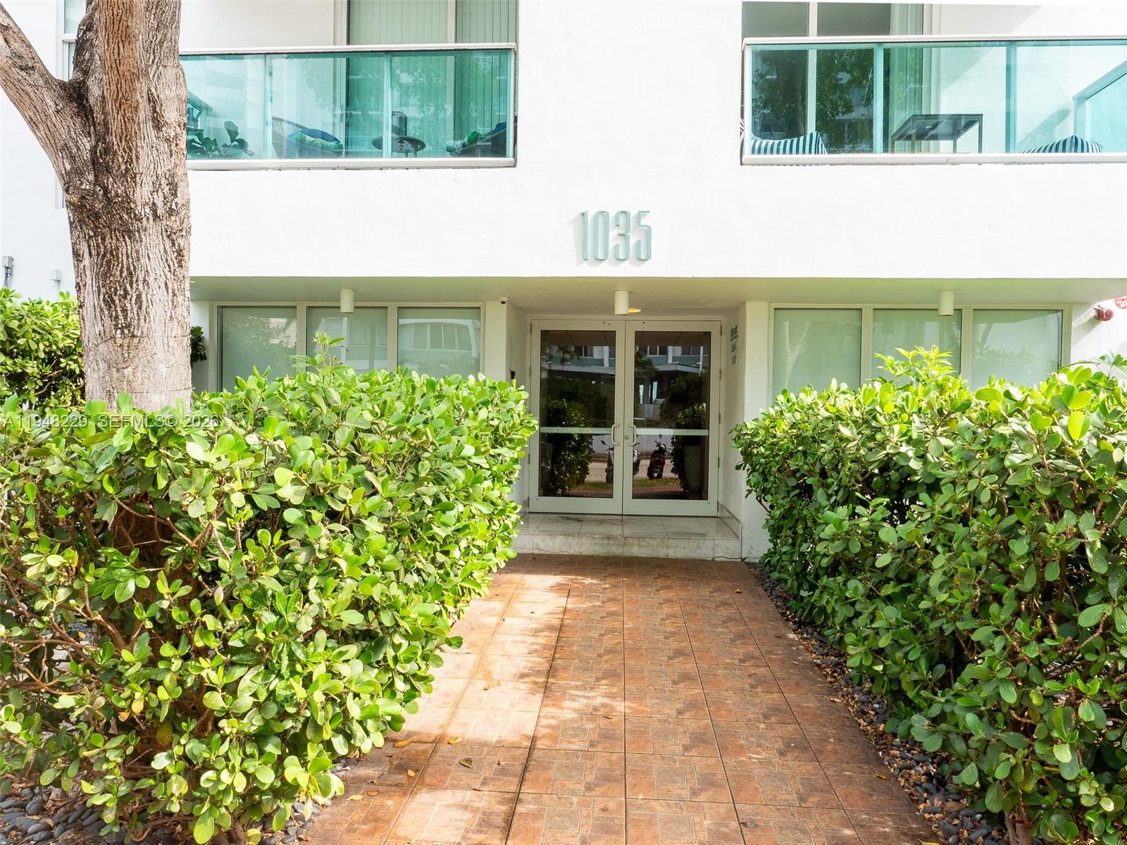 A paved walkway leads to the glass-paned entrance of a white building numbered 1035 — 1035 West Ave, Miami Beach FL 33139, MIAMI BEACH, FL