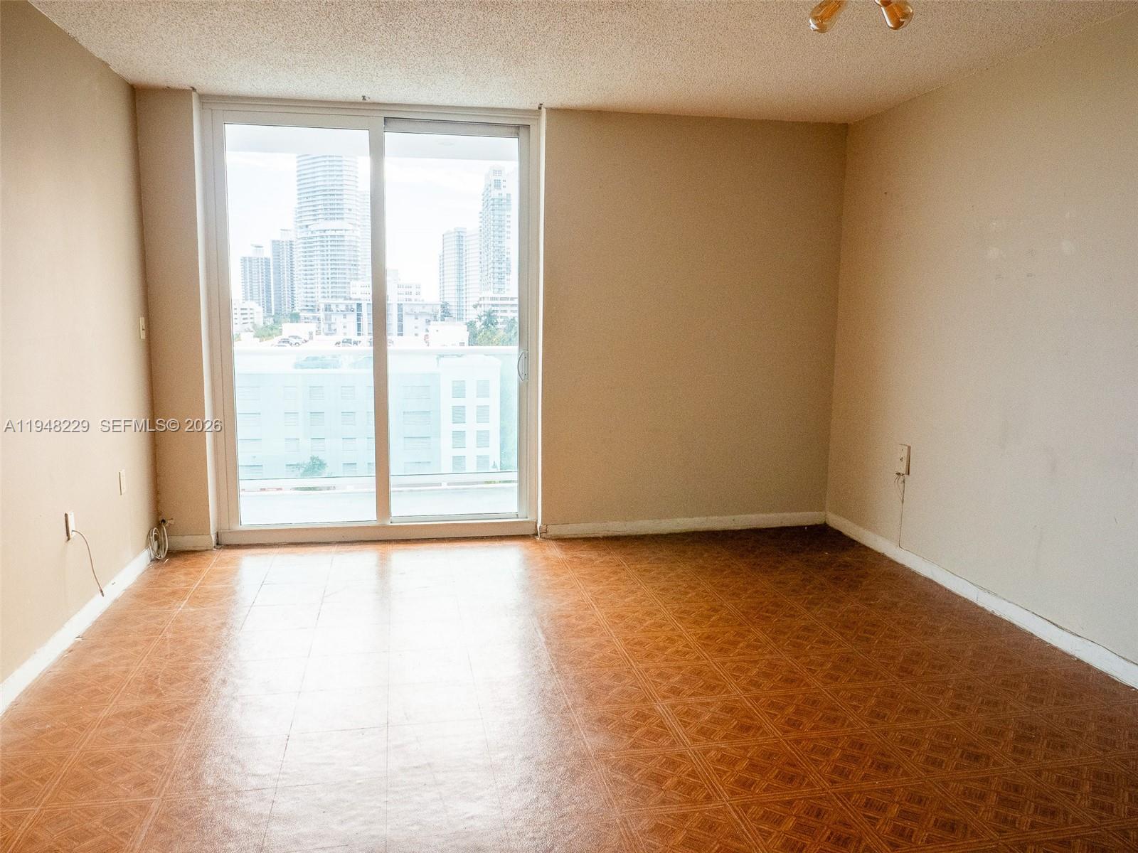 An empty room features brown patterned flooring, beige walls, and a sliding glass balcony door — 1035 West Ave, Miami Beach FL 33139, MIAMI BEACH, FL