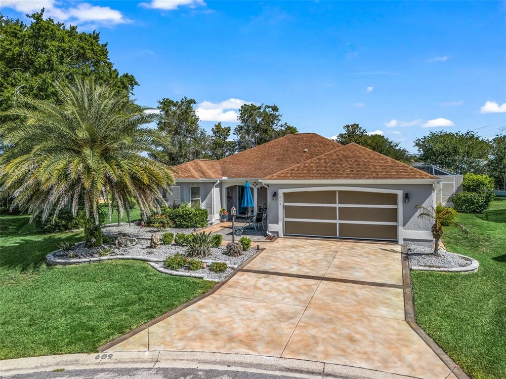 A single-story house with a brown roof, gray stucco, and a decorative concrete driveway — 609 ORTEGA WAY, THE VILLAGES, FL