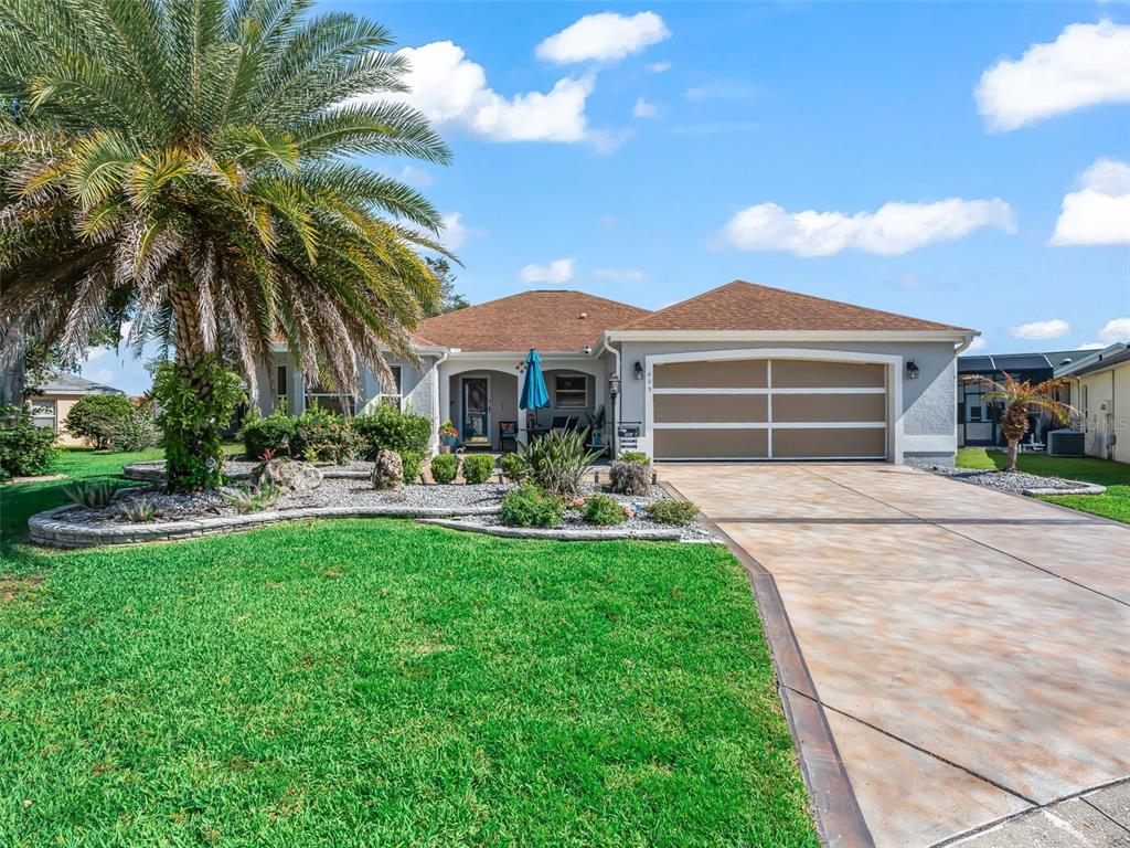 A single-story house with a tan garage, a palm tree, and a landscaped front yard — 609 ORTEGA WAY, THE VILLAGES, FL