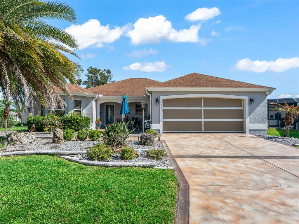 A single-story house with a tan garage, a palm tree, and a landscaped front yard — 609 ORTEGA WAY, THE VILLAGES, FL
