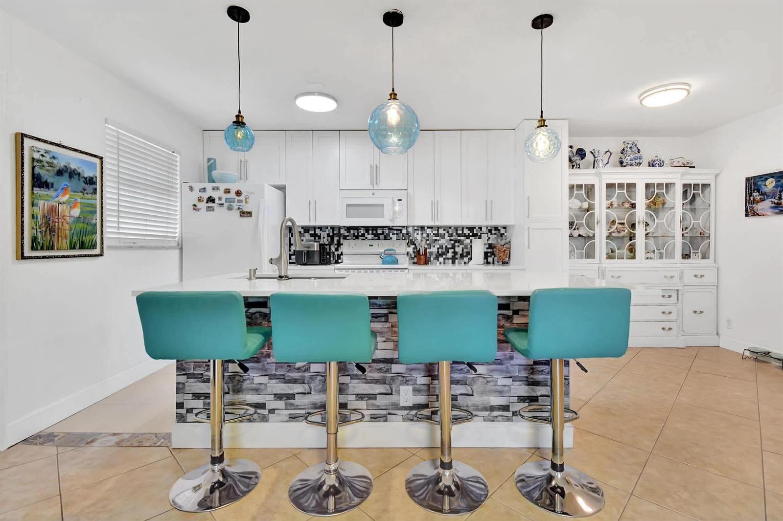 A kitchen features white cabinets, a stone-tiled island, and four teal bar stools — 1232 Club Drive W # D, Delray Beach FL 33445, DELRAY BEACH, FL