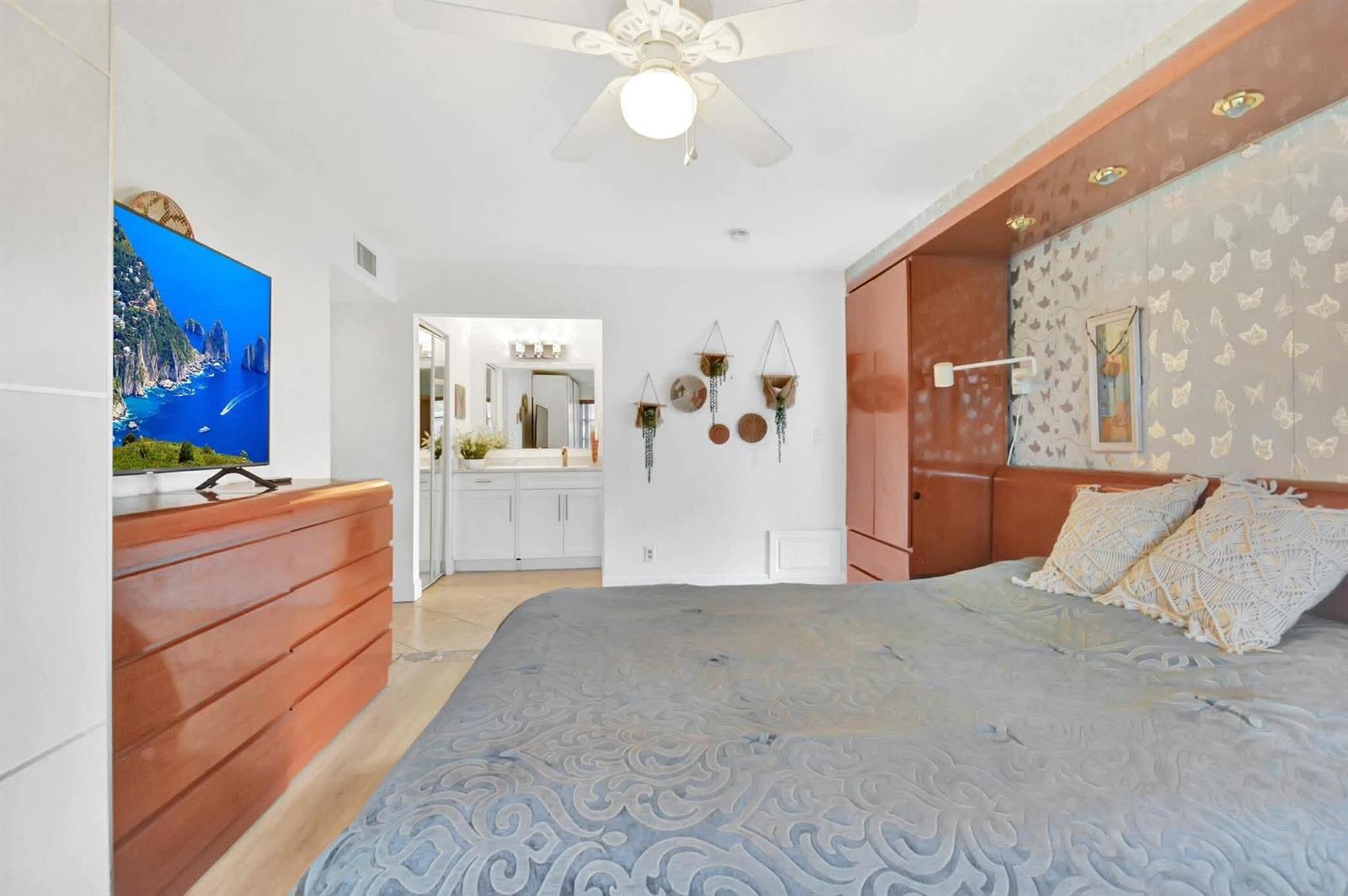 A bedroom features a wooden dresser, a television, a bed, and an attached bathroom — 1232 Club Drive W # D, Delray Beach FL 33445, DELRAY BEACH, FL