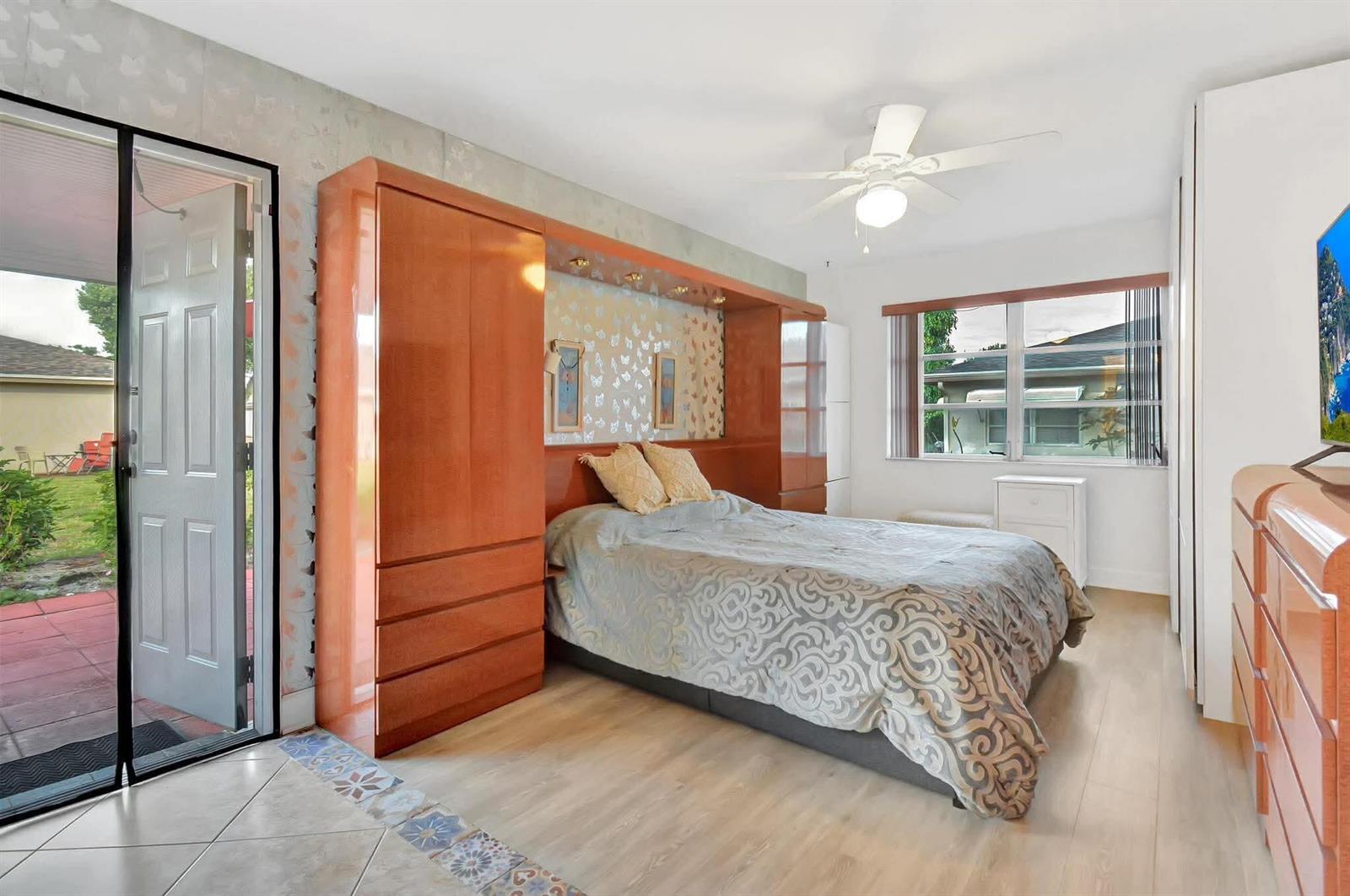 A bedroom features a built-in wooden headboard unit, a bed with patterned bedding, and a patio — 1232 Club Drive W # D, Delray Beach FL 33445, DELRAY BEACH, FL