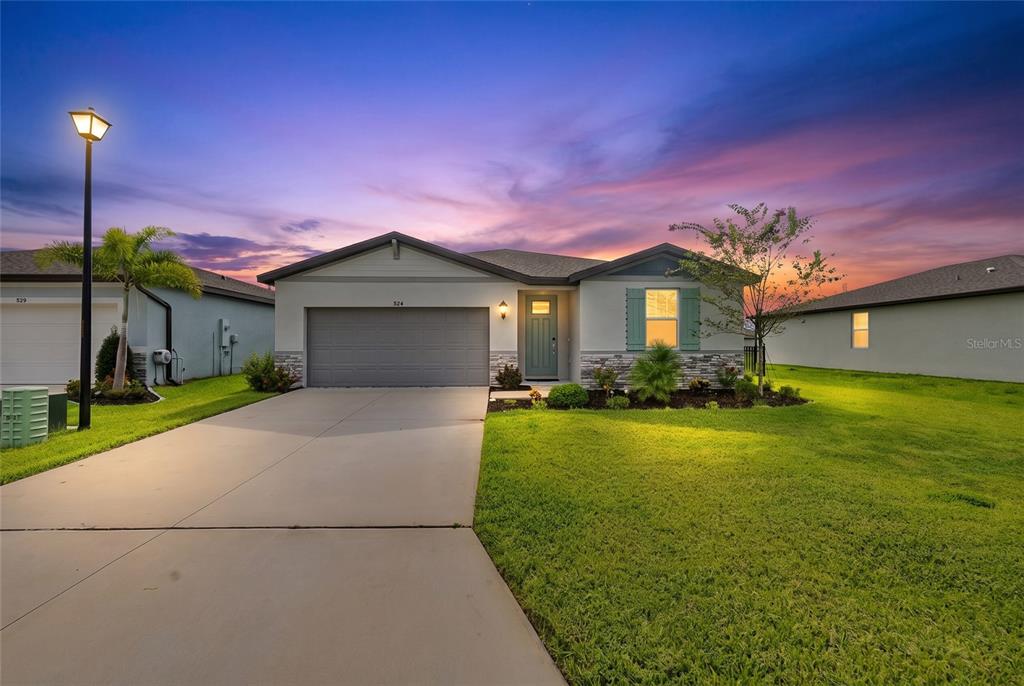 A single-story house with a gray garage, teal front door, and green lawn at sunset — 7124 AMELIA RIVER DRIVE, PARRISH, FL