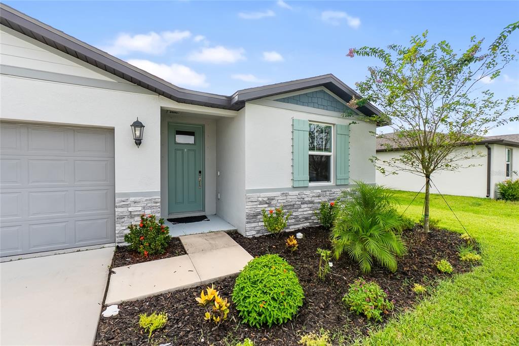 The exterior of a single-story house features a gray garage, a teal front door, and landscaping — 7124 AMELIA RIVER DRIVE, PARRISH, FL