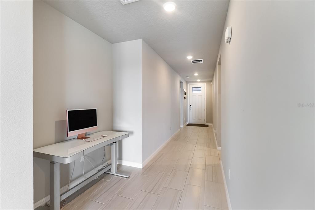 A hallway with light-colored tile flooring features a desk with a computer against the wall — 7124 AMELIA RIVER DRIVE, PARRISH, FL