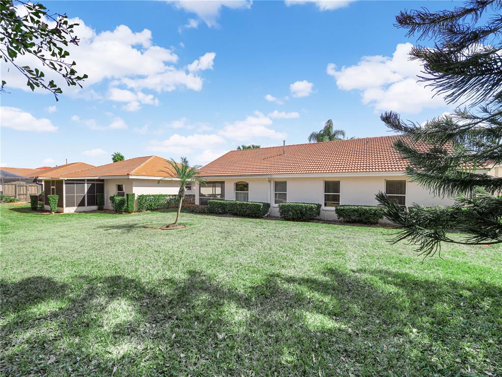 A backyard view of a single-story house with a tiled roof and green lawn — 528 GREENWAY DRIVE, LAKE WALES, FL