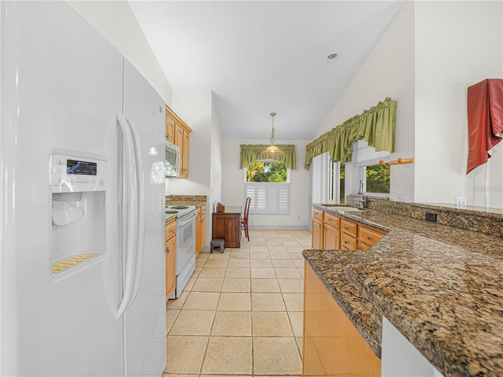 A kitchen features light wood cabinets, granite countertops, tile flooring, and a white refrigerator — 528 GREENWAY DRIVE, LAKE WALES, FL