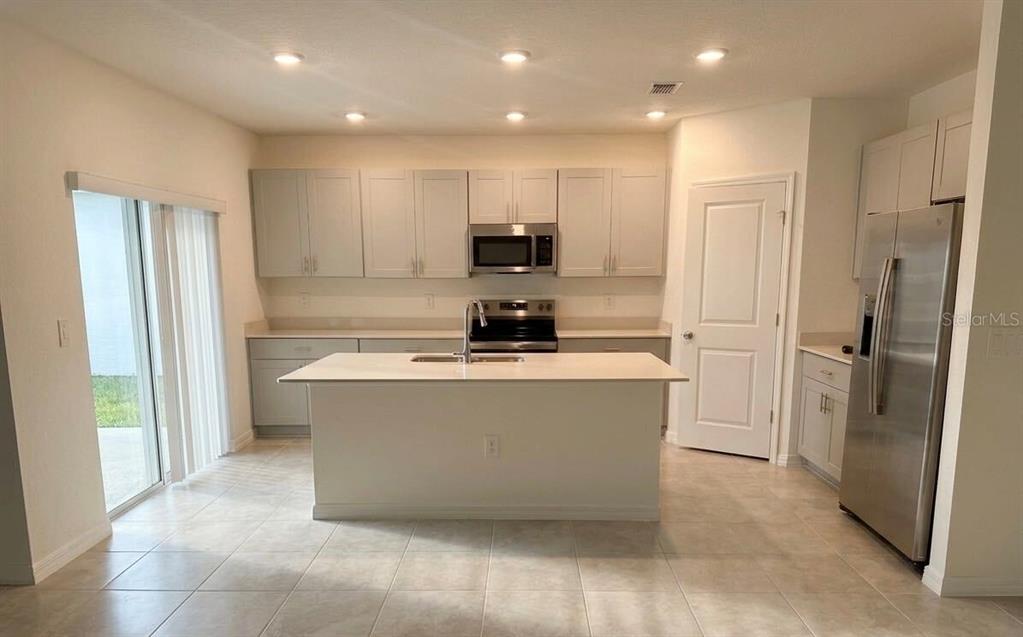 A kitchen with light gray cabinets, a white island, stainless steel appliances, and tile flooring — 5443 ISLA SAONA DRIVE, KISSIMMEE, FL