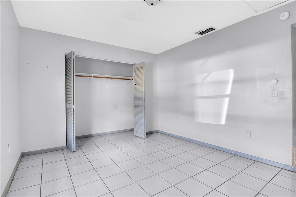 A bedroom with white walls, light-colored floor tiles, and an open louvered-door closet — 2464 CHESTNUT WOODS DRIVE, LAKELAND, FL