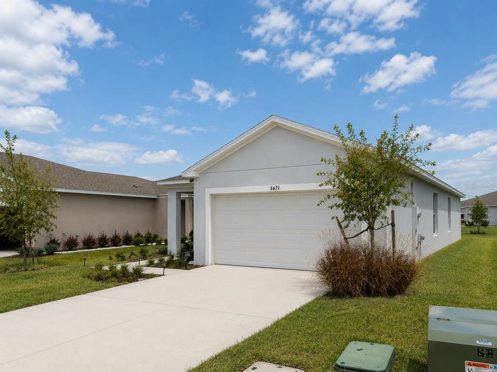 A single-story house with a white garage door and a concrete driveway under a blue sky — 5671 NISPERO WAY, KISSIMMEE, FL