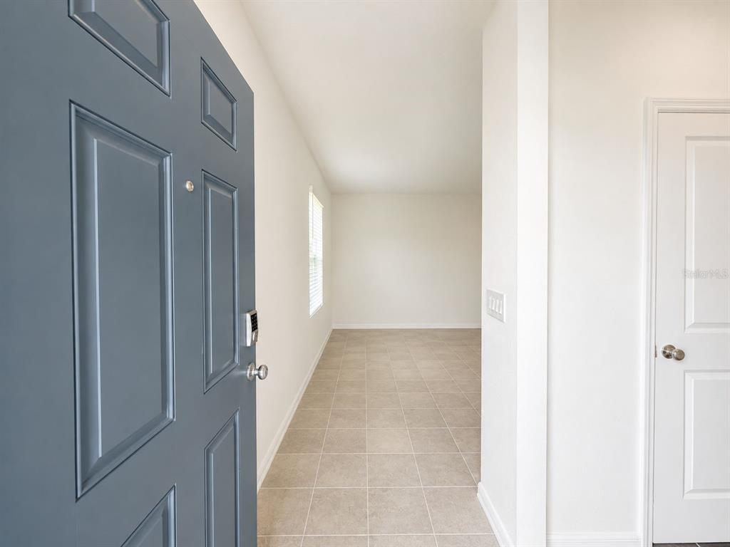 A blue front door opens into a tiled entryway with white walls and a door — 5671 NISPERO WAY, KISSIMMEE, FL