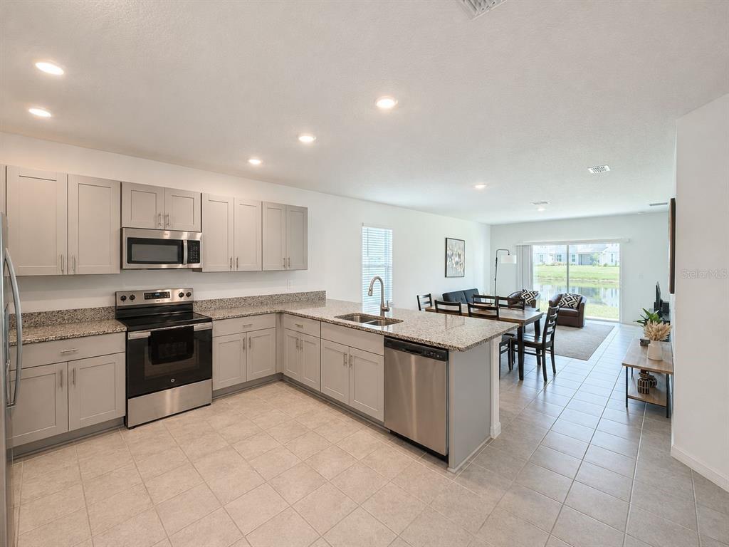 A kitchen with light gray cabinets, granite countertops, and stainless steel appliances overlooks a dining area — 5671 NISPERO WAY, KISSIMMEE, FL
