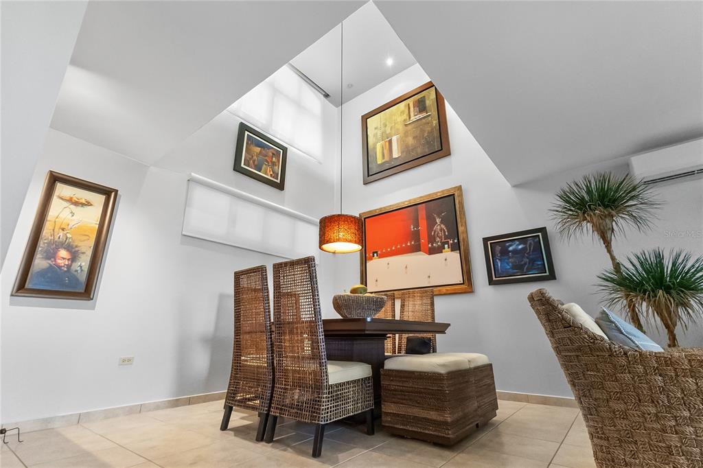 A dining area features wicker chairs, a wooden table, and artwork under a high skylight — 285 PALMAS INN WAY CORNER SE UNIT 1303, HUMACAO, PR