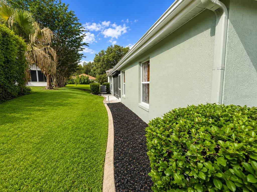 A side view of a light green house with a black mulch garden bed and lawn — 1211 CABELLA CIRCLE, LADY LAKE, FL