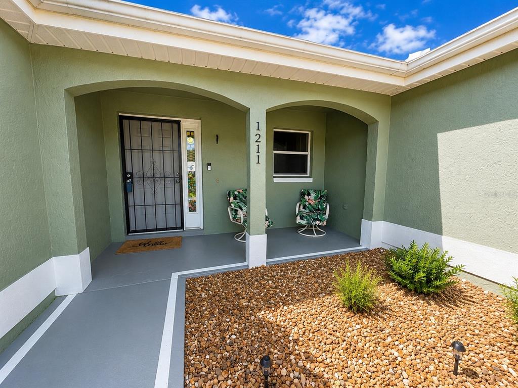 A covered entryway features a green exterior, a security door, and two chairs on a porch — 1211 CABELLA CIRCLE, LADY LAKE, FL