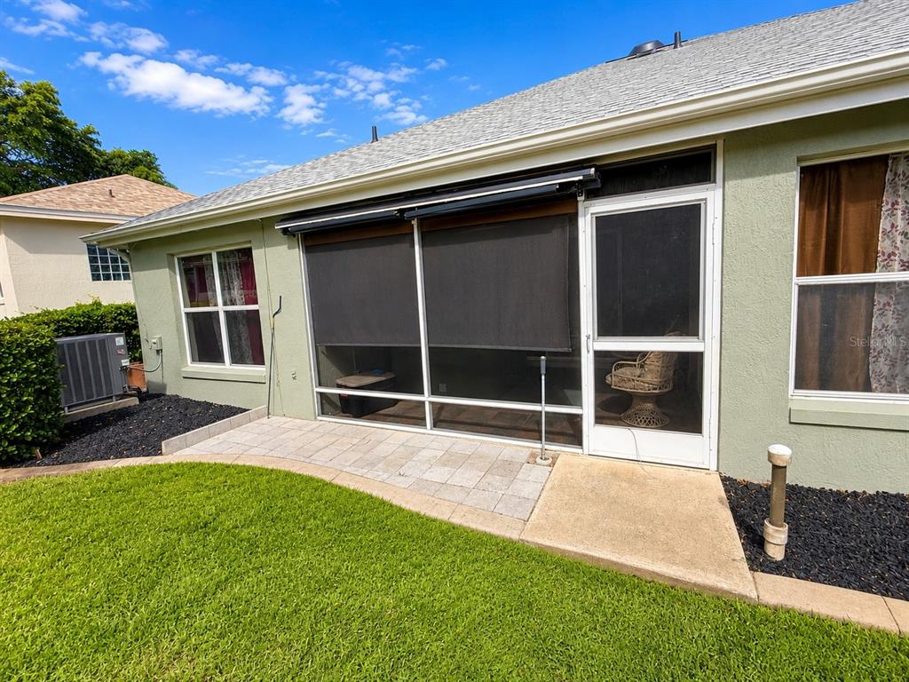 A paved patio area sits outside a screened-in porch with retractable shades on a house — 1211 CABELLA CIRCLE, LADY LAKE, FL