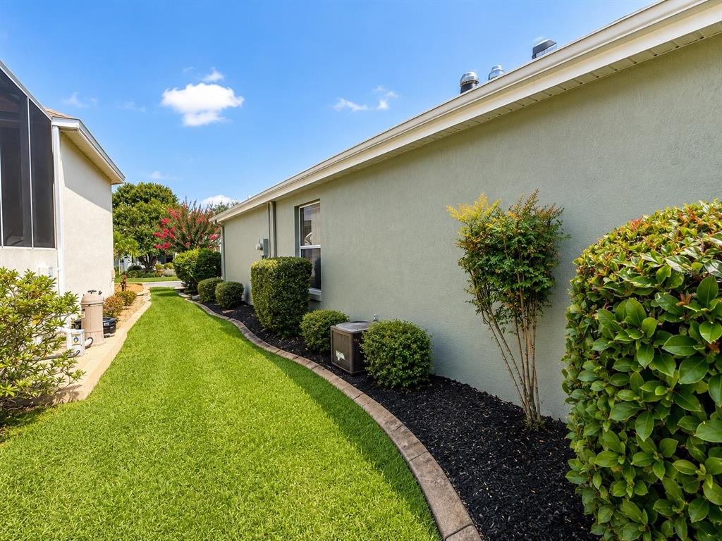 A side view of a light green house with a landscaped garden and lawn — 1211 CABELLA CIRCLE, LADY LAKE, FL