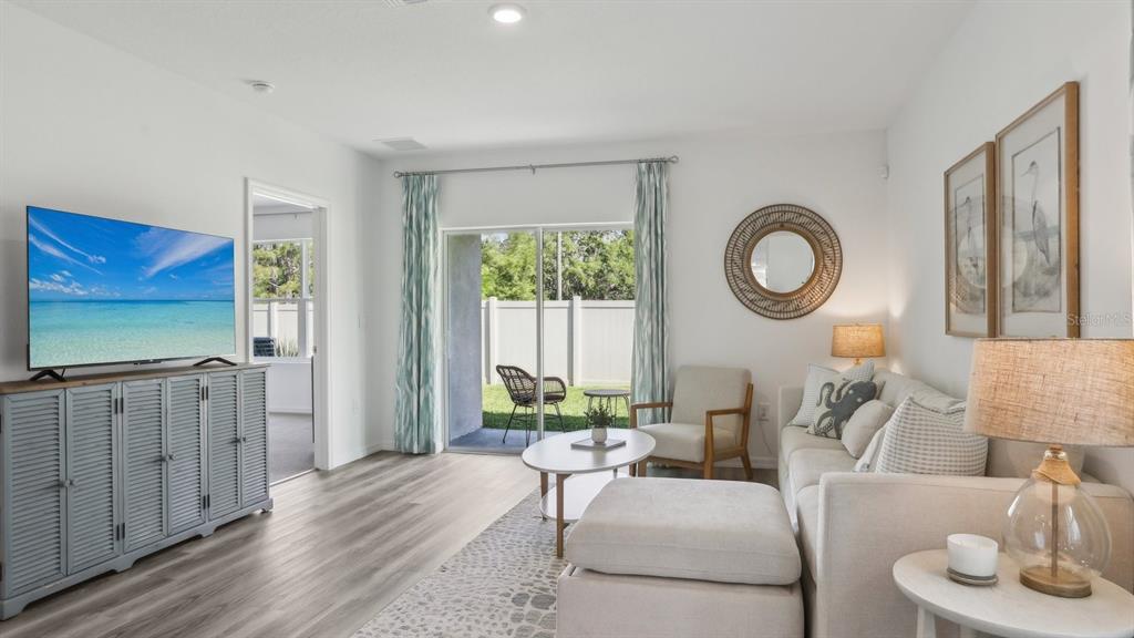 A living room features a television on a gray cabinet, sofa, and sliding glass doors — 32409 WEATHERED OAK DRIVE, WESLEY CHAPEL, FL