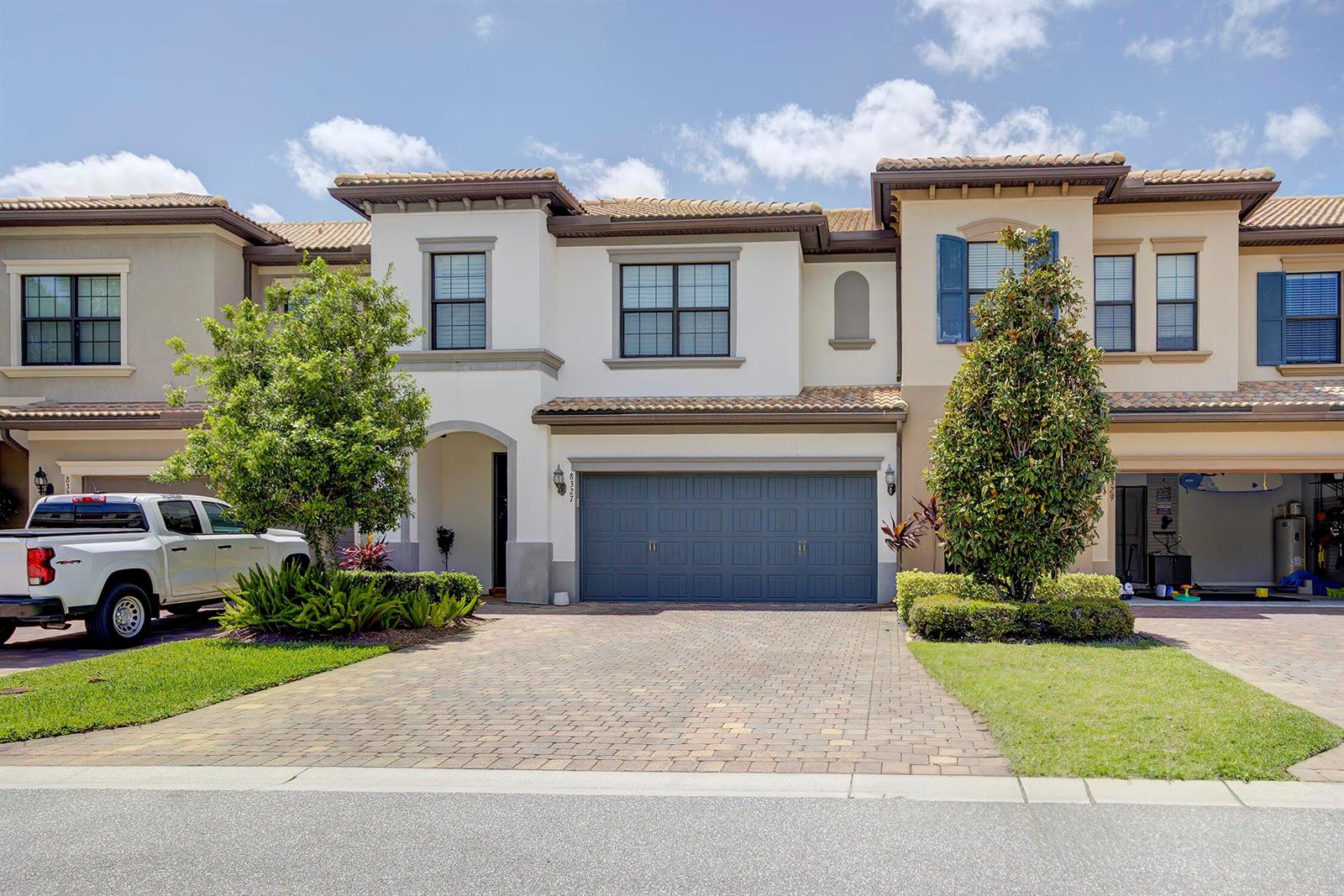 A two-story townhouse with a paved driveway, a blue garage door, and a white truck — 8327 Rearing Lane, Lake Worth FL 33467, LAKE WORTH, FL
