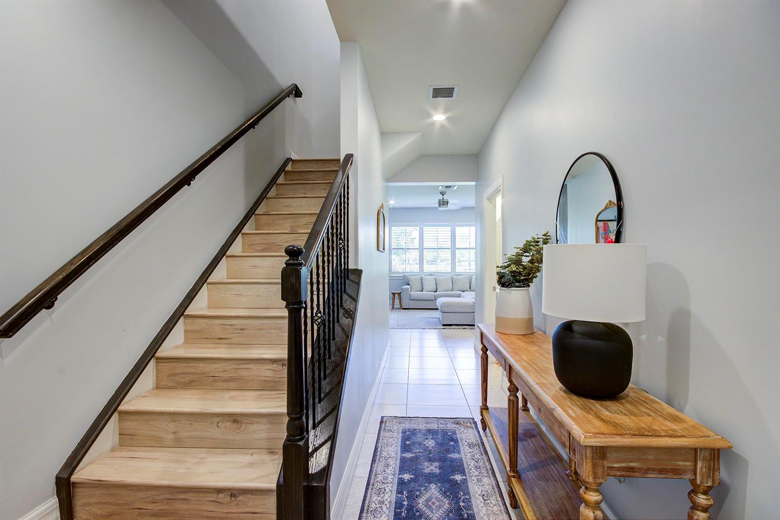 A hallway features a wooden staircase with a black railing, a console table, and tile flooring — 8327 Rearing Lane, Lake Worth FL 33467, LAKE WORTH, FL