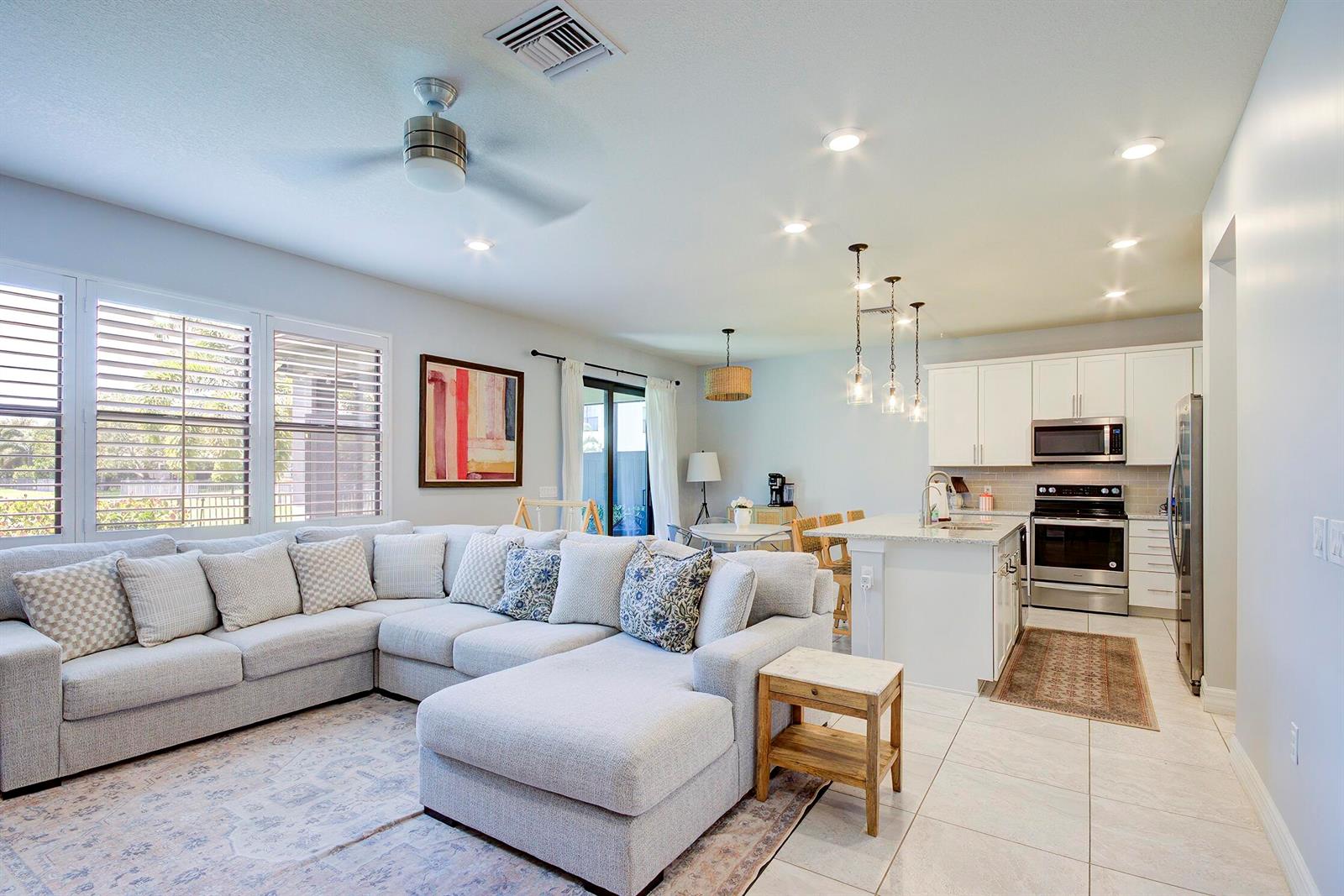 A bright open-concept living room and kitchen featuring a large sectional sofa and island — 8327 Rearing Lane, Lake Worth FL 33467, LAKE WORTH, FL